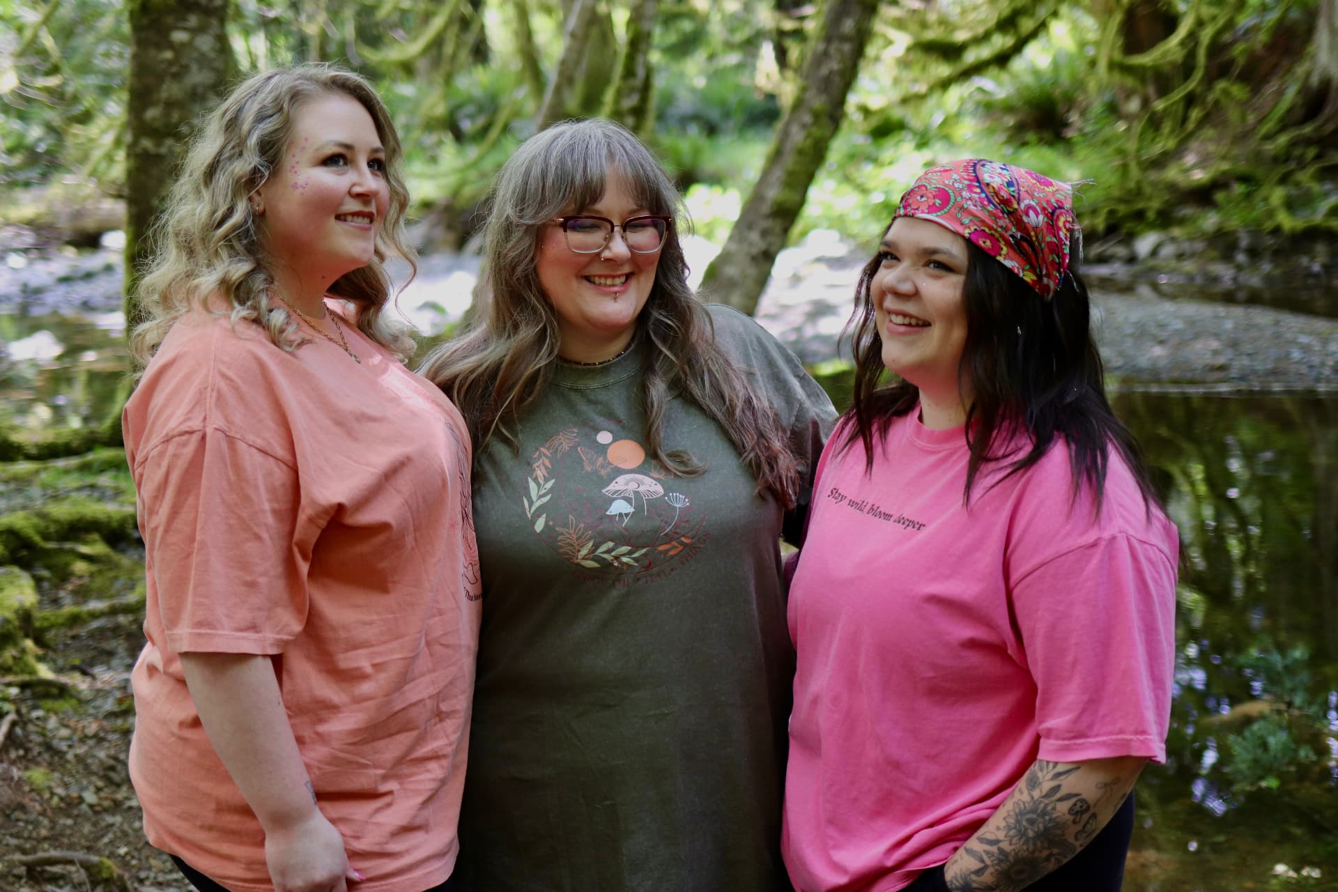 Three women smiling together in a mossy forest